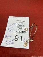 Wide shot of 10K gold necklace and two pendants alongside auction label with weight and description