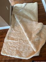 Sheepskin bed cover partially folded to show front side with plush cream sheepskin material and backing underneath.