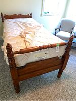 View of footboard of wooden single bed frame with mattress covered with a fitted sheet