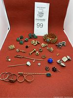 Full lot view showing variety of vintage jewelry including cufflinks, pins, rings, bracelet, and earrings arranged on red background.