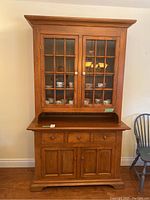 Full front view of vintage wooden buffet hutch showing upper glass-paneled cabinet with tea cups inside and lower cabinet with drawers and doors.