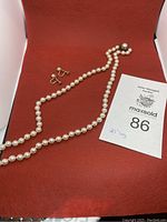 Pearl necklace and pair of pearl screw-back earrings displayed together on red fabric.