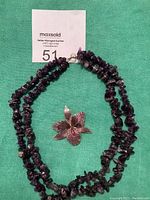 Full view of the double-strand amethyst necklace and purple trillium brooch on a green fabric background with auction lot number card.