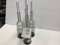 Four clear glass bottle lanterns with black metal handles and twine wraps, standing on white background for display.