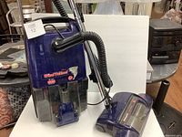 Full view of purple Hoover canister vacuum with attached hose and separate powered vacuum floor head.