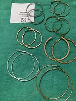 Overview photo showing 7 pairs of hoop earrings in silver and gold tones arranged on green fabric