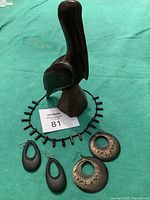 Pelican sculpture with two pairs of earrings and black coral necklace arranged on green fabric.