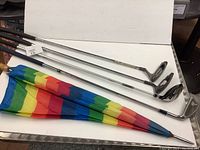 Five golf items laid flat: two putters, one 4 wood, one wedge, and a rainbow striped golf umbrella with wood handle.