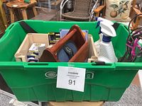Green plastic bin containing various household items including light bulbs, spray bottle, and wooden shoe shine kit.