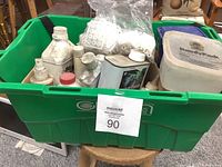 Green bin filled with various bottles and containers of cleaners, paint thinner, and other liquids.