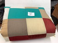 Folded handmade quilt with visible patchwork squares in teal, beige, gray, cream, red colors, showing various textures and fabrics.