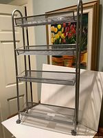 Front view of the 4-tier metal shelving unit showing the four removable mesh basket shelves and caster wheels.