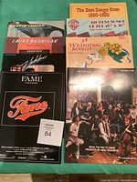 Photo showing the full lot of 8 music books arranged in a pile, displaying the front covers with a variety of titles and designs related to piano, vocal, and guitar sheet music.