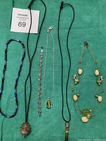 Full view of five necklaces and one bracelet laid flat on a green background showing details and length variance