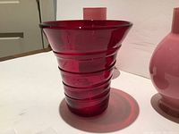 Close-up of the cranberry red glass vase showing fluted top and ridged body design.