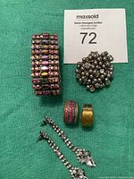 Full set showing bracelet, three rings, and earrings on green background with auction label.