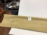 Faux grass cloth roller shade laid flat on table. Natural beige color with woven texture look, pull cord attached.