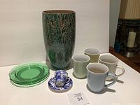 Full lot showing abstract vase, green glass plates, blue and white Royal Crown Derby tea cup and saucer, plus four assorted mugs.