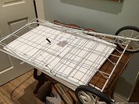 Top view showing white metal grid wire basket of the cart along with large black & white wheels beneath.