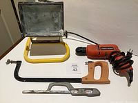 Full lot of tools including Black & Decker drill, drywall saw, hacksaw, and work light on floor for display.
