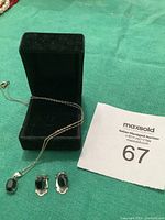 Photo of the necklace with fine silver chain and black tourmaline pendant alongside matching clip-on earrings displayed in a black jewelry box