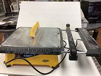 Front view of the QEP 650XT wet saw showing the yellow base, metal cutting table with ruler, and black handle assembly.