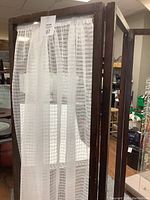 Front view of wood frame privacy screen with white sheer curtains hung on each panel.