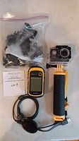 Garmin eTrex 10 handheld GPS in yellow and black with 2.2-inch monochrome display, Apeman underwater camera mounted on yellow waterproof hand grip, and a bag of camera accessories including mounts and cables.