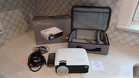 Apeman LC350 projector with power cable, remote control, carrying case, and original box on table.
