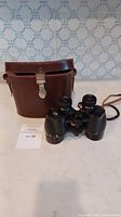 Vintage 9x35 Solaross binoculars in front of brown leather carrying case on countertop.