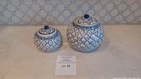 Photo showing both blue and white decorative ceramic jars with lids on a marble surface, emphasizing size and pattern.