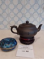Chinese Yixing clay teapot with calligraphy on wooden stand next to a cloisonné enamel decorative box