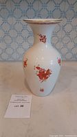 Full view of the Herend Hungarian porcelain vase with orange floral designs on a white textured background.