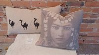 Two cushions displayed against a brick wall: one rectangular with black camel silhouettes; one square with Indian woman portrait in grayscale.