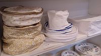 Three stacked fabric quilted china storage cases on shelf, two with floral pattern, one white.