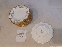Set of 14 Royal Crown Derby Normandie pattern bread plates stacked on each other with one plate bottom visible showing the manufacturer's stamp.