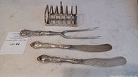 Photo showing two silver spreaders, a carving fork, and a toast rack all placed on a flat surface to illustrate the lot contents and condition.