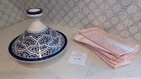 Photo of the blue and white ceramic tagine and pink damask napkins folded next to each other on a marble surface.