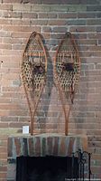 Front view of both snowshoes mounted vertically on brick wall, showing full length and shape.