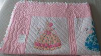 Full view of folded quilt showing pink border and Sunbonnet Girl appliqués.