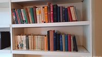 Wide view of two shelves filled with vintage and antique hardcover books in varied spine colors and sizes, showing the extent of the collection.