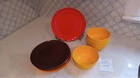 Set of three color groups of vintage melamine plates and bowls. Includes brown and orange plates, yellow bowls and plates, arranged on a counter with natural light.
