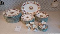 Full set view showing stacked dinner plates, smaller plates, bowls, oval platter at the back, 4 demi tasse cups, and 8 saucers all with floral and gold trim design.