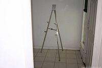 Full view of the aluminum folding easel standing upright on a tiled floor against a white wall.