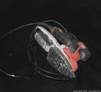 Detail sander with black and red body and triangular sanding pad showing heavy dust and wear.