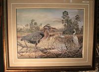 Photo showing framed print artwork featuring herons and wetland plants, signed by Robert Binks.