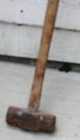 Photo showing close-up of heavy sledge hammer head and wooden handle, heavily used.