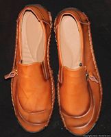 Top view of a pair of light brown leather slip-on casual shoes showing symmetrical design and detailed stitching.