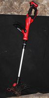 Photo of the rechargeable cordless weed eater showing the red and black body with ergonomic handle, secondary grip, and attached battery pack at the top.