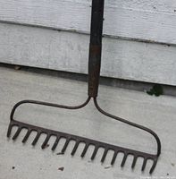 Close-up photo of a metal garden rake with multiple tines and a black handle showing rust and wear.